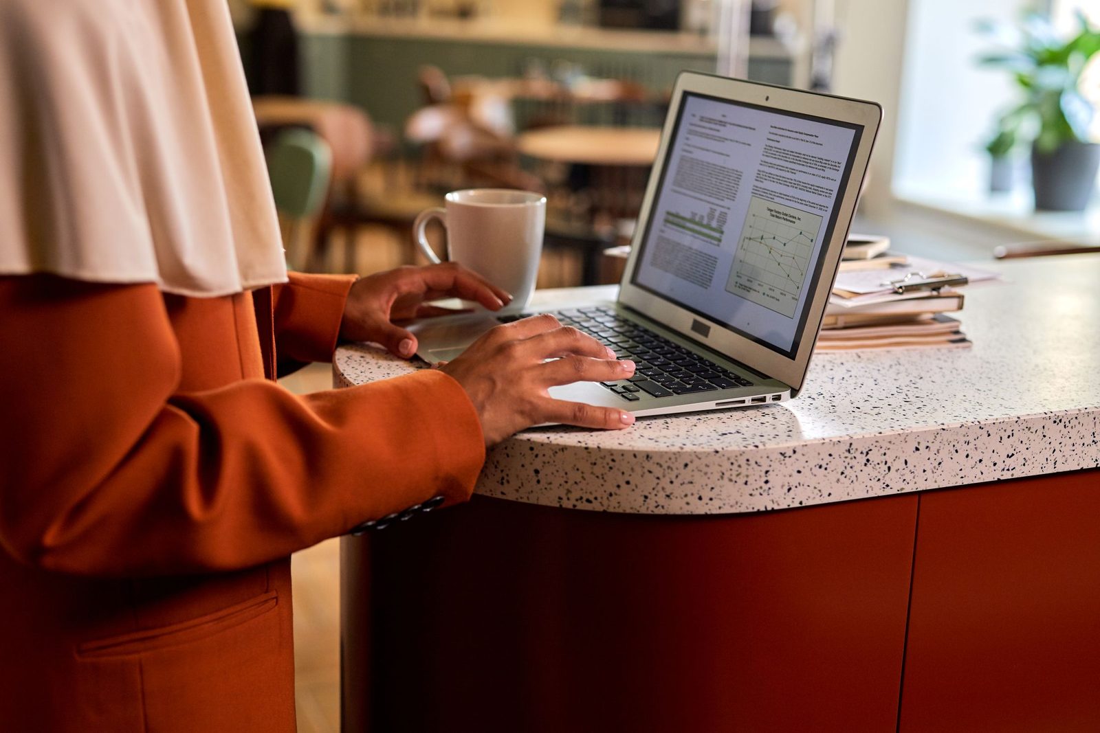 A woman typing on a laptop at a counter with a coffee beside her