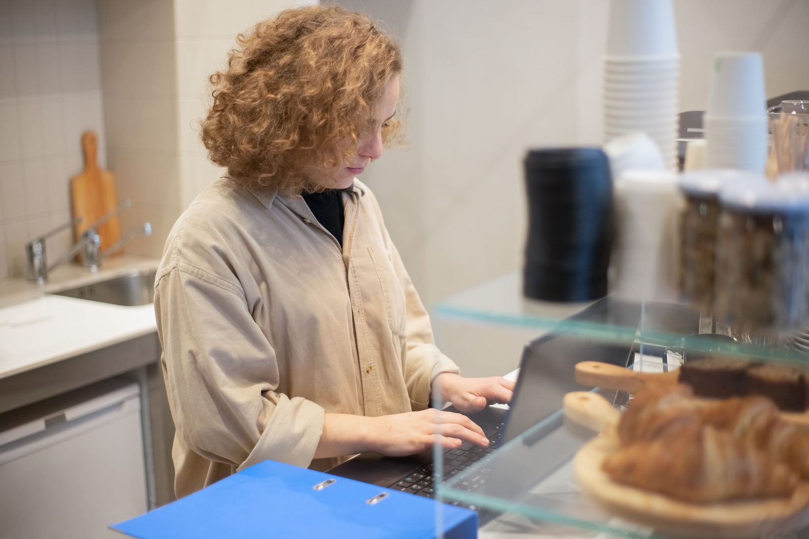 A café owner using a laptop behind the counter, with pastries in front