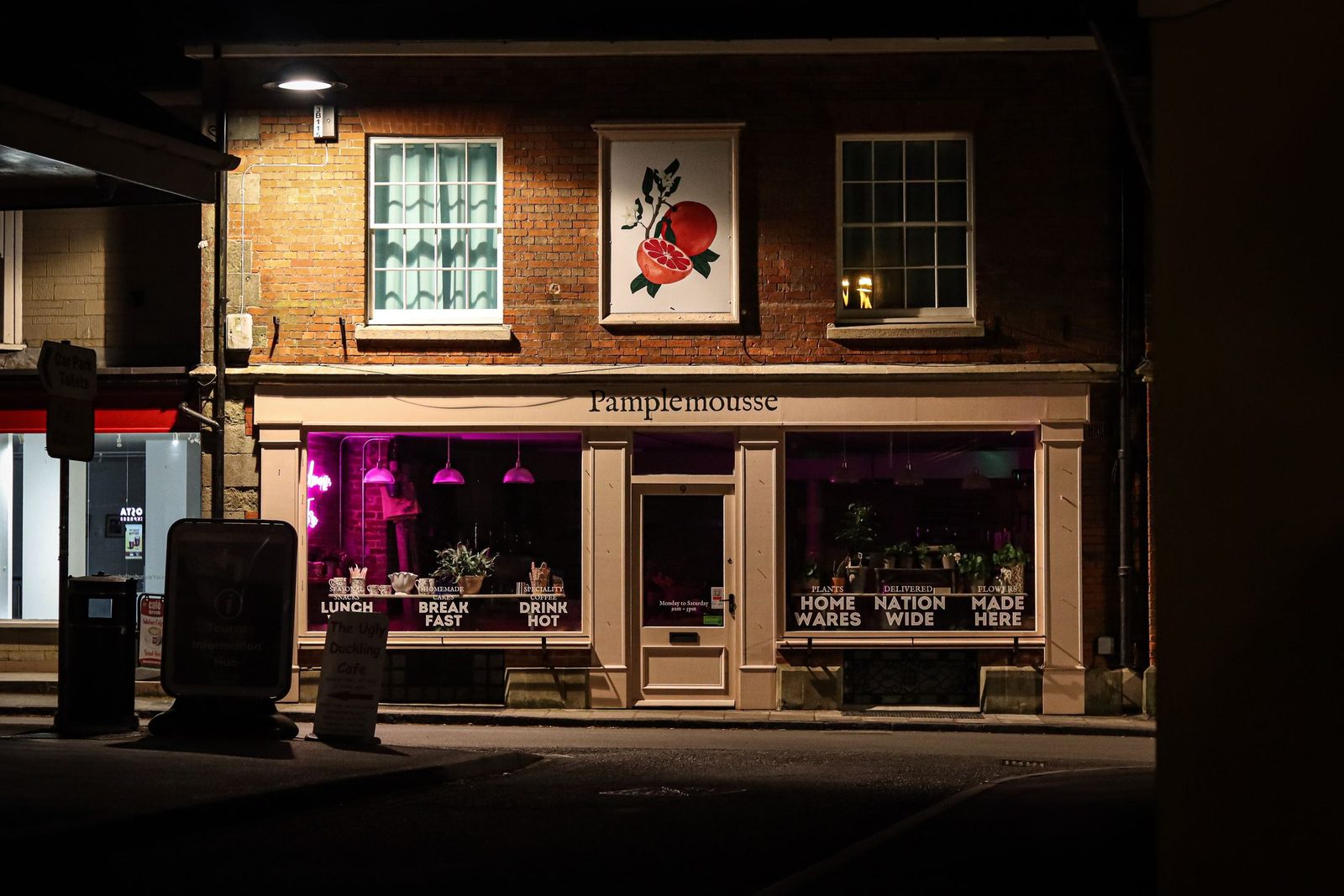 A lit-up independent shopfront on a street in Shaftesbury, England, in the evening